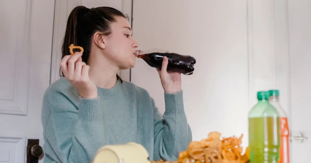 Mulher exausta após chegar do serviço, comendo alimentos industrializados por impulso, ansiedade e estresse.