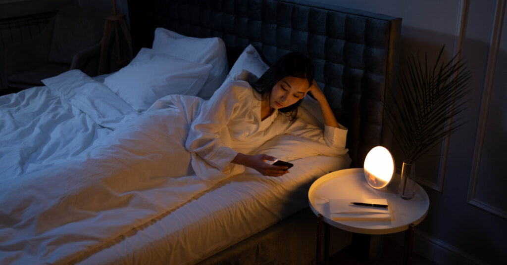 Mulher com insônia no celular sofrendo com o impacto do sono ruim no emagrecimento feminino.