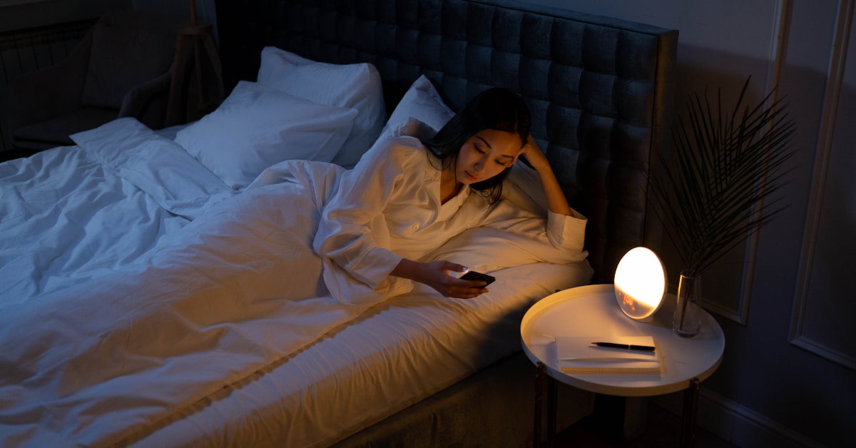 Mulher com insônia no celular sofrendo com o impacto do sono ruim no emagrecimento feminino.